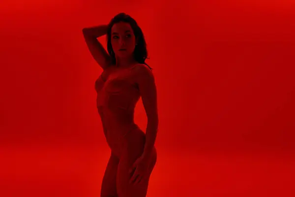 Una joven posa seductora frente a un vibrante fondo rojo. - foto de stock