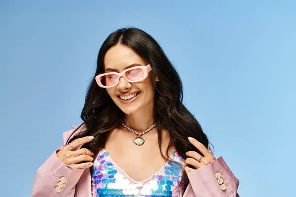 Une femme à la mode rayonne d'une ambiance estivale dans une veste rose et des lunettes de soleil roses sur fond de studio bleu. — Photo de stock