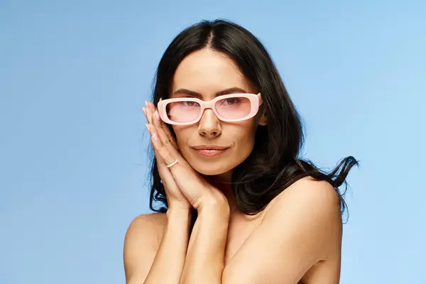 A stylish woman is striking a pose in pink sunglasses against a blue studio backdrop, embodying summertime vibes. — Stock Photo