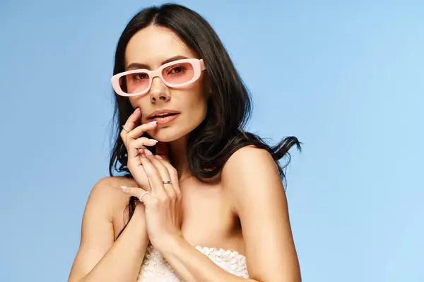 A stylish woman donning pink sunglasses strikes a pose for a portrait in a studio against a vibrant blue backdrop. — Stock Photo