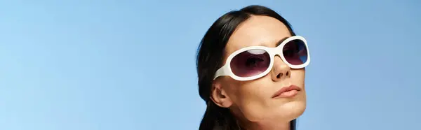 A glamorous woman wearing sunglasses looks up into the sky against a blue studio backdrop. — Stock Photo