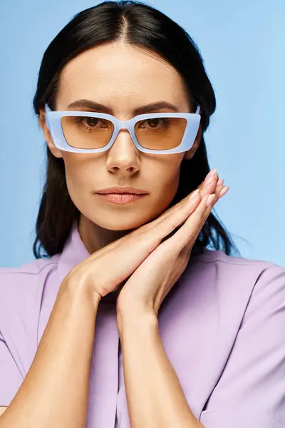 A fashionable woman in purple shirt and chic glasses poses in a studio with a summertime vibe against a blue backdrop. — Stock Photo