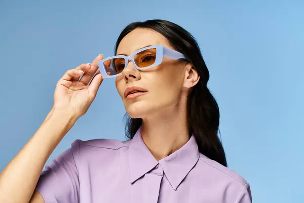 A stylish woman wearing a purple shirt and sunglasses poses confidently against a vibrant blue background in a studio setting. — Stock Photo
