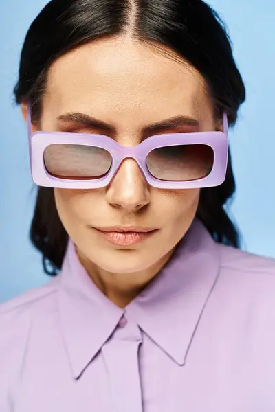 A fashionable woman exudes summertime vibes in a purple shirt and matching sunglasses against a blue studio backdrop. — Stock Photo