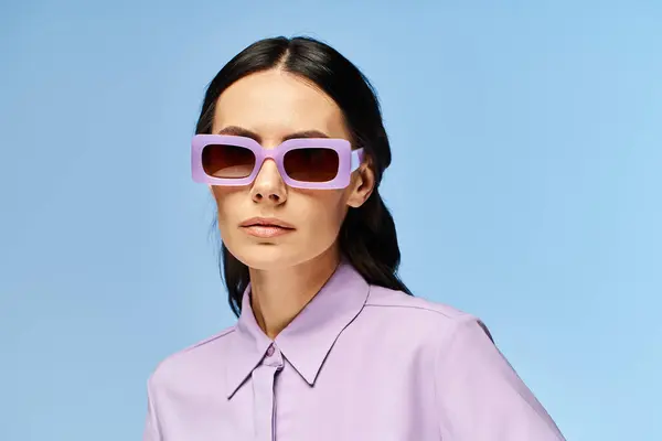 Uma mulher na moda está desfrutando das vibrações de verão, vestindo trajes roxos e óculos de sol na moda contra um fundo de estúdio azul. — Fotografia de Stock