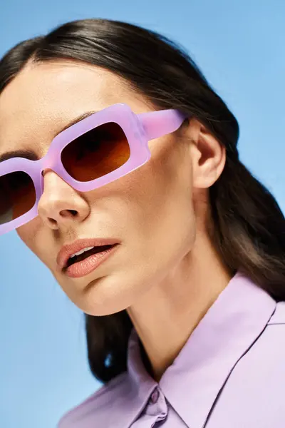A fashionable woman with a purple shirt and trendy sunglasses posing in a studio with a summertime vibe on a blue background. — Stock Photo
