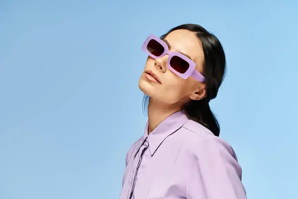 A stylish woman with purple sunglasses and shirt poses against a blue backdrop in a summery studio setting. — Stock Photo