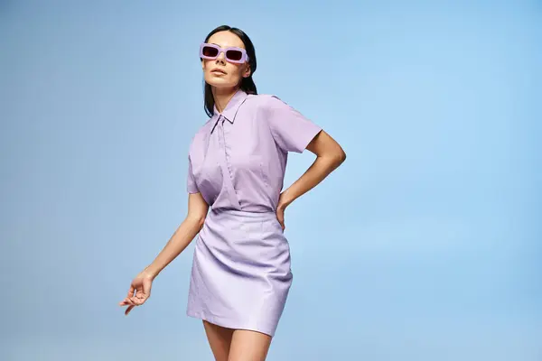 A beautiful woman in a purple dress and stylish sunglasses poses in a studio against a summery blue background. — Stock Photo