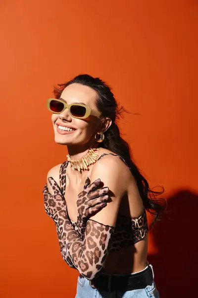 Uma mulher elegante exibe moda verão em uma camisa de impressão de leopardo e óculos de sol na moda contra um pano de fundo laranja. — Fotografia de Stock