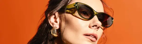 Una mujer elegante con gafas de sol redondas sobre un fondo naranja que emana vibraciones de moda veraniega. - foto de stock