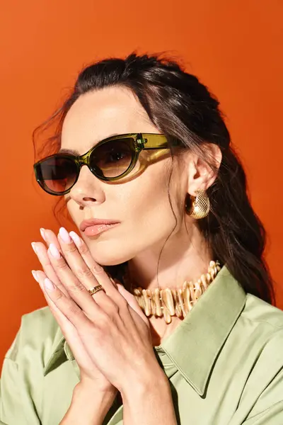A stylish woman wearing sunglasses and praying, showcasing summertime fashion on an orange background. — Stock Photo