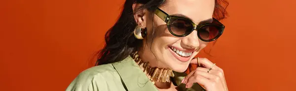 Модная женщина в солнечных очках и ожерелье, излучающая летние вибрации в студии на оранжевом фоне. — стоковое фото