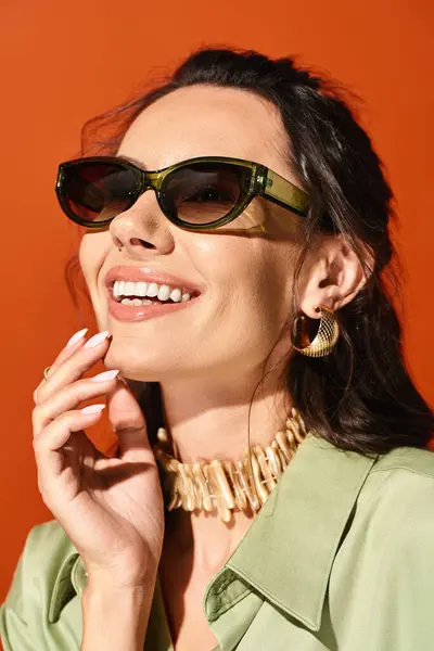 Стильна жінка викриває літню моду в сонцезахисних окулярах і заяву намисто на помаранчевому фоні. — стокове фото