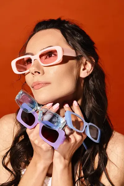 Une femme à la mode avec des vibrations estivales porte des lunettes de soleil roses et bleues sur fond orange. — Photo de stock