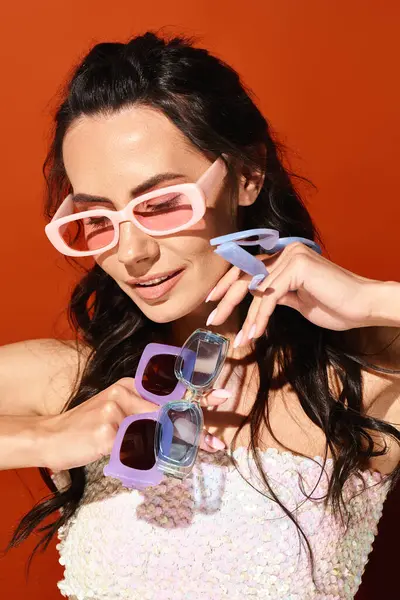 A fashionable woman in a white dress and pink sunglasses posing in a studio on an orange background, exuding summertime style. — Stock Photo