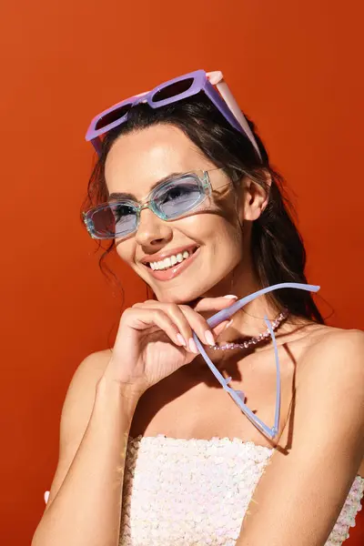 A fashionable woman exudes elegance in a white dress and sunglasses, standing confidently in a studio with a warm orange background. — Stock Photo
