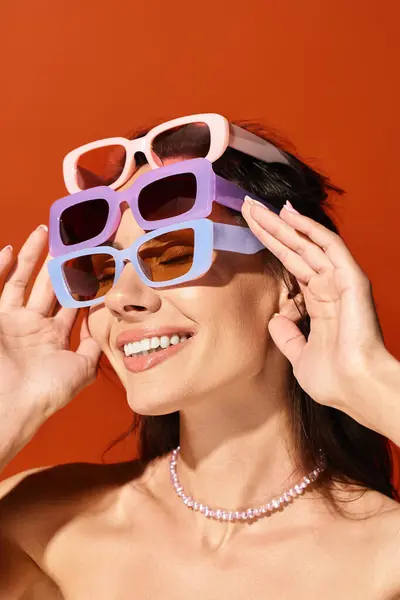 Una mujer de moda vistiendo gafas de sol y un collar, exudando confianza en un estudio brillante sobre un fondo naranja. - foto de stock