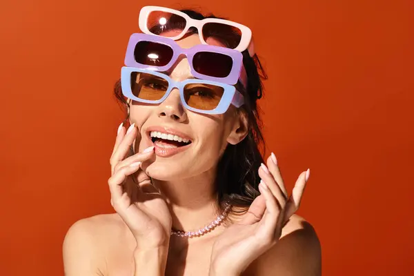 Una mujer de moda posando con gafas de sol posadas sobre su cabeza sobre un fondo naranja. - foto de stock