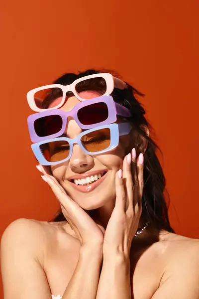 Une femme élégante avec des lunettes de soleil frappant une pose dans un studio, sur un fond orange, respirant les vibrations de la mode estivale. — Photo de stock