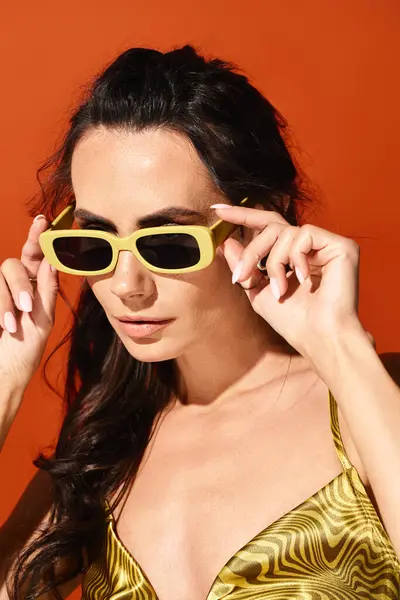 A stylish woman with a radiant smile wears a vibrant yellow top and trendy sunglasses against a bold orange backdrop. — Stock Photo