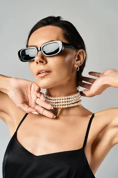 Uma mulher na moda exalando estilo em óculos de sol e uma gargantilha contra um fundo de estúdio cinza. — Fotografia de Stock