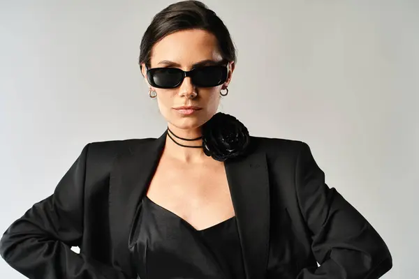Стильная женщина в черном костюме и солнечных очках уверенно позирует в студии на сером фоне. — стоковое фото