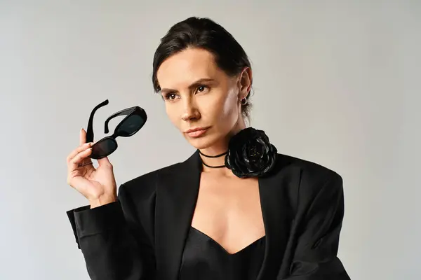 A fashionable woman in a sleek black suit confidently holds up a pair of chic sunglasses, exuding a sense of sophistication and style. — Stock Photo