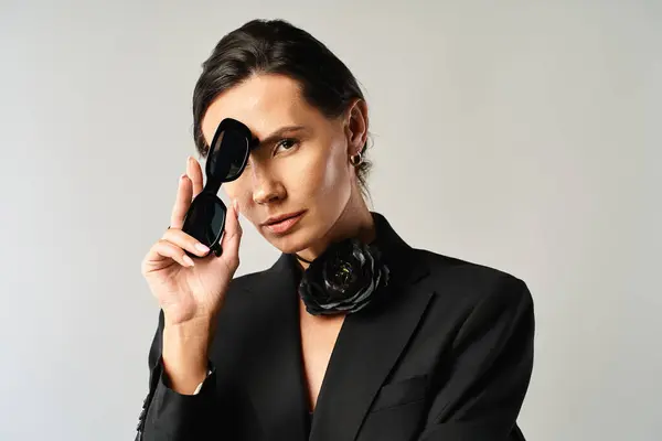 Una mujer con estilo en un traje con confianza sostiene un par de gafas de sol negras en un entorno de estudio - foto de stock