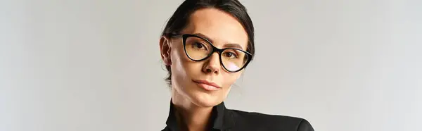 Una mujer de moda exuda sofisticación en una camisa negra, complementada con gafas de sol elegantes, contra un fondo de estudio neutral. - foto de stock