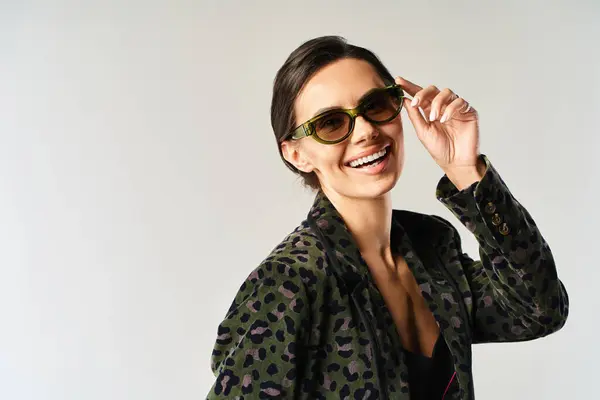 Une femme élégante pose dans une veste imprimée léopard et des lunettes de soleil à la mode sur fond de studio gris. — Photo de stock