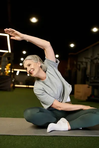 Lebenslustige attraktive Seniorin in bequemer Sportbekleidung mit grauen Haaren, die im Fitnessstudio ihre Muskeln dehnt — Stockfoto