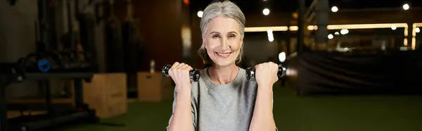 Allegra bella donna anziana in accogliente abbigliamento sportivo esercizio con manubri e sorridente alla macchina fotografica, banner — Foto stock