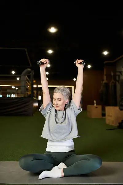 Cheerful attractive mature sportswoman with gray hair exercising actively with dumbbells in gym — Stock Photo