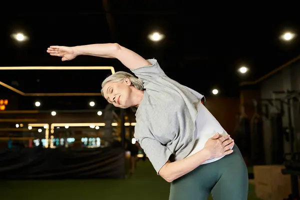Gioiosa attraente sportiva matura in abito accogliente allungando i muscoli durante l'esercizio in palestra — Foto stock