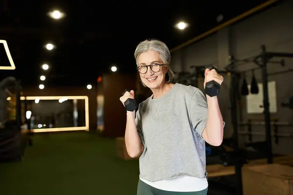 Cheerful senior sportswoman with gray hair exercising with dumbbells and smiling at camera — Stock Photo