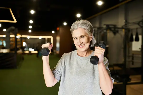 Cheerful appealing mature sportswoman with gray hair exercising with dumbbells and looking at camera — Stock Photo