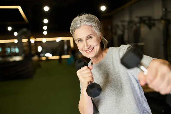 Attraente donna anziana felice in formazione abbigliamento sportivo attivamente con manubri e sorridente alla fotocamera — Foto stock