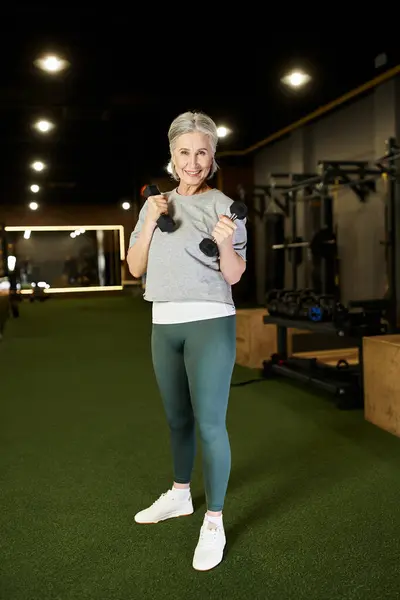 Positive good looking senior woman in sportswear exercising with dumbbells and looking at camera — Stock Photo