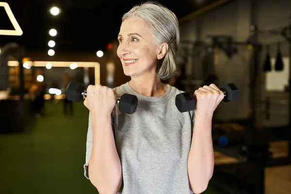 Good looking mature sportswoman in cozy attire exercising actively with dumbbells while in gym — Stock Photo