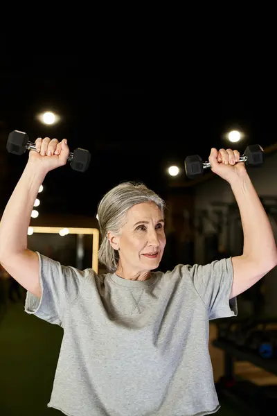Attraktive Seniorin in kuscheliger Sportkleidung, die im Fitnessstudio aktiv mit Kurzhanteln trainiert — Stockfoto