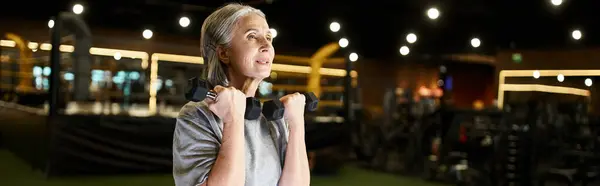 Schöne reife Sportlerin in bequemer Kleidung, die hart mit Hanteln trainiert, während sie im Fitnessstudio ist, Banner — Stockfoto