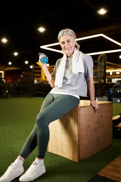 Gioiosa sportiva anziana con asciugamano e bottiglia sorridente alla macchina fotografica mentre si rilassa dopo l'allenamento — Foto stock