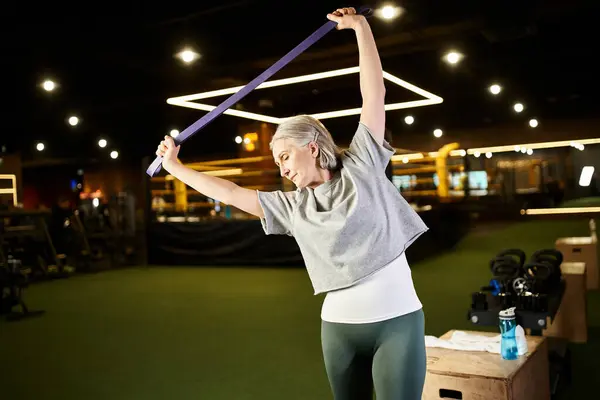 Joyful senior sportswoman in comfy attire exercising actively with fitness expander while in gym — Stock Photo