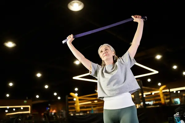 Merry mature good looking sportswoman in cozy attire training with fitness expander while in gym — Stock Photo