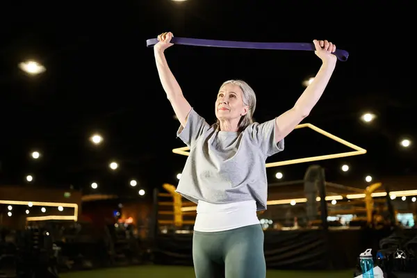 Sonriente sénior hermosa deportista en cómodo entrenamiento de atuendo con expansor de fitness mientras está en el gimnasio - foto de stock