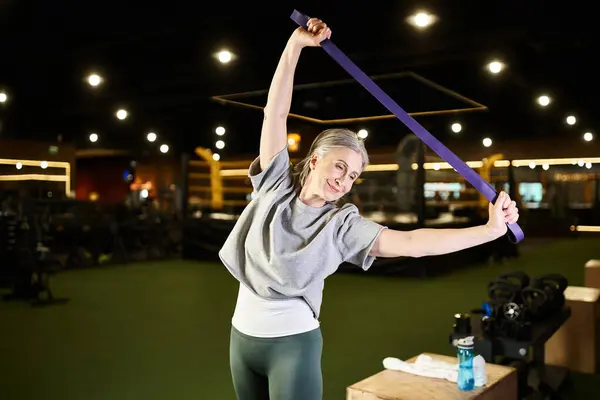 Jolly mature beautiful sportswoman in cozy attire training with fitness expander while in gym — Stock Photo