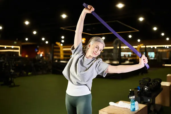 Alegre madura hermosa deportista en acogedor entrenamiento de atuendo con expansor de fitness mientras está en el gimnasio - foto de stock