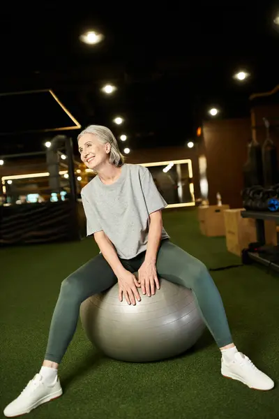 Jolly donna matura in abbigliamento sportivo in posa con espansore fitness e sacchetto di peso e sorridente alla macchina fotografica — Foto stock