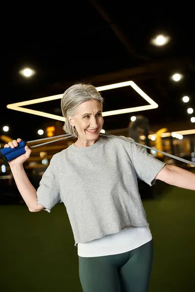 Allegra anziana bella donna in abbigliamento sportivo in posa con corda da salto in palestra e guardando altrove — Foto stock