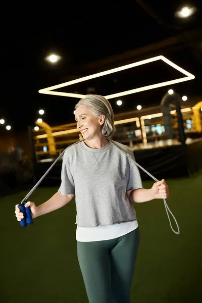 Jolly senior attractive sportswoman in comfy attire posing with skipping rope and looking away — Stock Photo